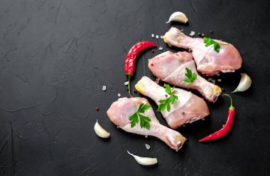 Baharat, biber ve maydanoz yaprakları ile tavuk bacakları siyah taş arka plan üzerinde