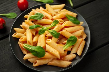 Ahşap arka plan üzerinde domates sosu ve yeşil yaprakları ile Makarna 