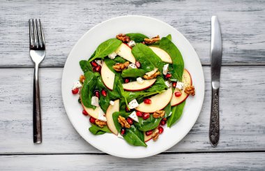 Ahşap arka plan üzerinde ıspanak yaprakları, peynir, nar tohumu, elma dilimleri ve fındık ile taze salata 