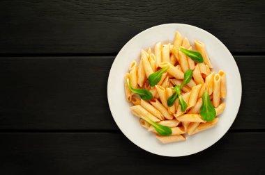 taş siyah arka plan üzerinde yeşil yaprakları ile servis domates soslu makarna