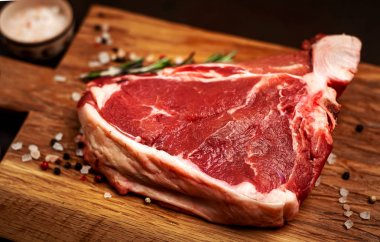 Taş arka plan üzerinde ahşap doğrama tahtası üzerinde baharat ve biberiye dal ile Çiğ yağlı biftek