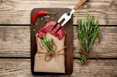 Ahşap doğrama tahtası üzerinde biberiye dalları ile zanaat kağıt sarılmış çiğ sığır eti biftek