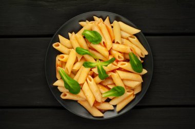 taş siyah arka plan üzerinde yeşil yaprakları ile servis domates soslu makarna