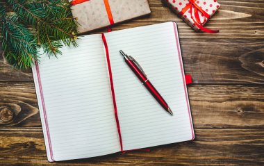 Eski ahşap arka plan üzerinde kırmızı yay ve boş defter ile hediye kutuları yığını 