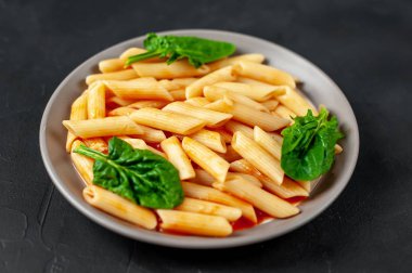 taş siyah arka plan üzerinde yeşil yaprakları ile servis domates soslu makarna