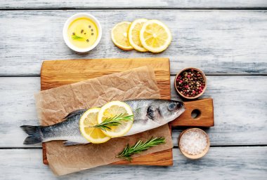 Ahşap doğrama tahtası üzerinde limon dilimleri ve biberiye dalları ile çiğ balık