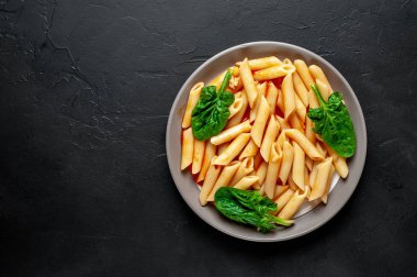 taş siyah arka plan üzerinde yeşil yaprakları ile servis domates soslu makarna