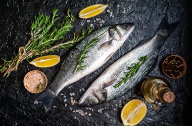 Siyah taş arka plan üzerinde limon, baharat ve biberiye dalları ile çiğ balık