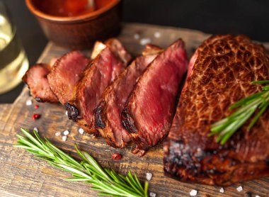 Ahşap doğrama tahtası üzerinde biberiye dalları ile dilimlenmiş orta nadir sığır eti biftek yakın görünümü