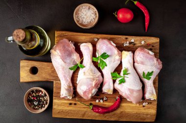 Siyah taş arka plan üzerinde ahşap doğrama tahtası üzerinde baharat, tuz, maydanoz yaprakları ve yağ şişesi ile Tavuk bacakları