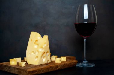 Ahşap tahta üzerinde Maasdam peynirsiyah taş arka plan üzerinde kırmızı şarap ile servis 