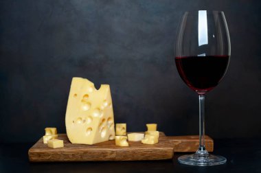 Ahşap tahta üzerinde Maasdam peynirsiyah taş arka plan üzerinde kırmızı şarap ile servis 