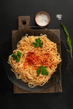 koyu taş arka plan üzerinde domates sosu ve maydanoz yaprakları ile İtalyan spagetti makarna