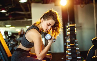 Spor salonunda dambılla egzersiz yapan genç bir kadın.