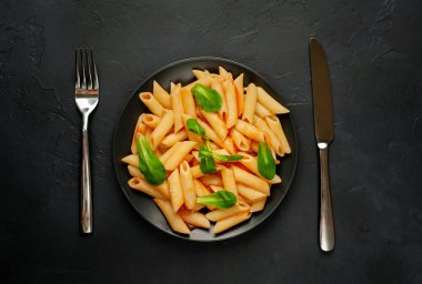 taş siyah arka plan üzerinde yeşil yaprakları ile servis domates soslu makarna