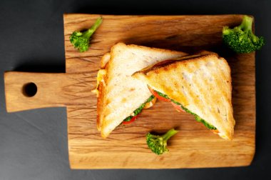 Ahşap doğrama tahtasında jambon, taze brokoli ve peynirile taze ızgara sandviçler