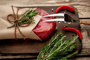 Ahşap doğrama tahtası üzerinde biberiye dalları ile zanaat kağıt sarılmış çiğ sığır eti biftek