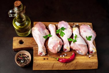 Siyah taş arka plan üzerinde ahşap doğrama tahtası üzerinde baharat, tuz, maydanoz yaprakları ve yağ şişesi ile Tavuk bacakları