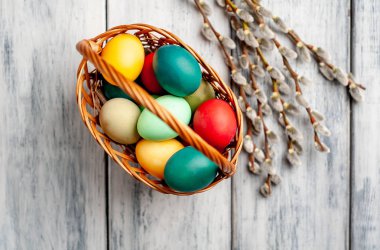 Beyaz ahşap arka planda renkli Paskalya yumurtaları ve kedi söğüt dalları ile sepet