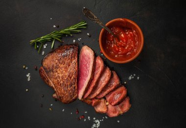 Dilimlenmiş taze sığır eti biftek taş arka plan üzerinde domates sosu ve biberiye dal ile servis