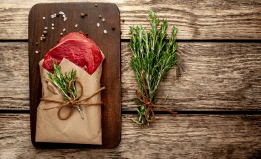 Ahşap doğrama tahtası üzerinde biberiye dalları ile zanaat kağıt sarılmış çiğ sığır eti biftek