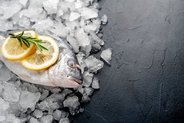 Soğuk ezilmiş buz yığını üzerinde limon dilimleri ve biberiye ile taze balık yakın görünümü