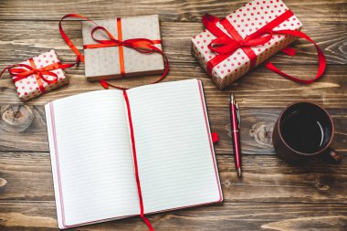 Eski ahşap arka plan üzerinde kırmızı yay ve boş defter ile hediye kutuları yığını 