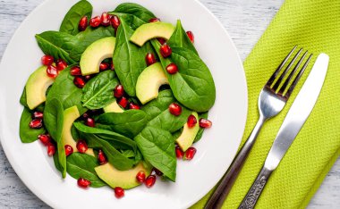 Ahşap masada ıspanak yaprakları, avokado dilimleri ve nar taneleri ile taze yeşil salata 