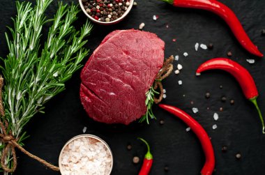 Siyah taş arka plan üzerinde yeşil biberiye dalları ve baharatlar ile Çiğ biftek 