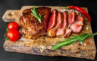 Ahşap doğrama tahtası üzerinde biberiye dalları ile dilimlenmiş orta nadir sığır eti biftek yakın görünümü