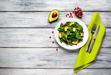 Ahşap masada ıspanak yaprakları, avokado dilimleri ve nar taneleri ile taze yeşil salata 
