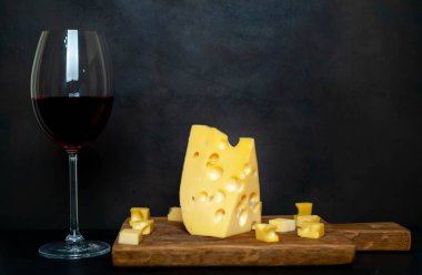 Ahşap tahta üzerinde Maasdam peynirsiyah taş arka plan üzerinde kırmızı şarap ile servis 