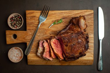 Siyah taş arka plan üzerinde ahşap doğrama tahtası üzerinde baharat ile Yağlı ızgara domuz biftek
