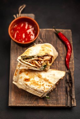 Ahşap doğrama tahtası üzerinde baharatlı sos ile tavuk ve sebze ile sarılmış geleneksel Meksika burrito 