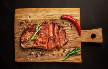 Siyah taş arka plan üzerinde ahşap doğrama tahtası üzerinde baharat ve biberiye dalları ile Taze ızgara domuz biftek