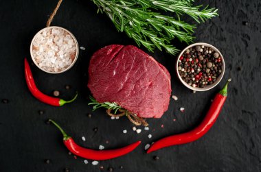 Siyah taş arka plan üzerinde yeşil biberiye dalları ve baharatlar ile Çiğ biftek 