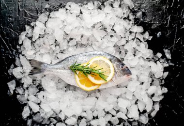 Soğuk ezilmiş buz yığını üzerinde limon dilimleri ve biberiye ile taze balık yakın görünümü
