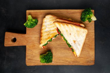 Ahşap doğrama tahtasında jambon, taze brokoli ve peynirile taze ızgara sandviçler