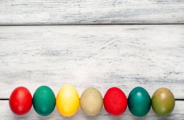 Beyaz ahşap arka planda renkli Paskalya yumurtaları yığını