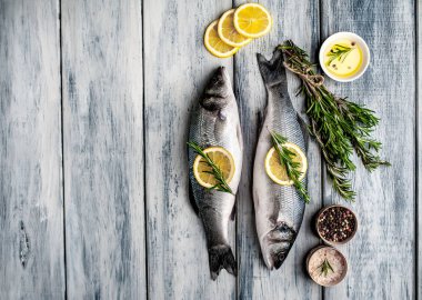 Gri ahşap arka plan üzerinde limon dilimleri ve biberiye dalları ile çiğ balık