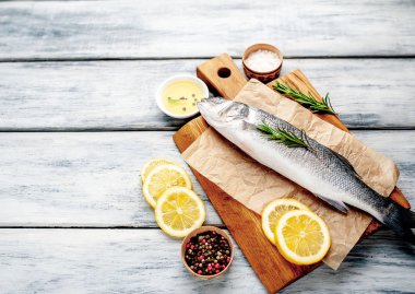 Ahşap doğrama tahtası üzerinde limon dilimleri ve biberiye dalları ile çiğ balık
