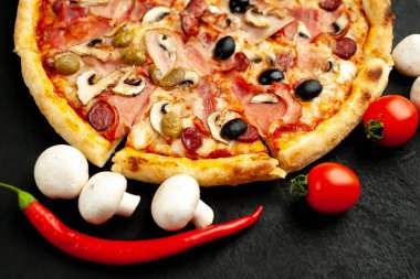 Siyah taş arka plan üzerinde mantar, domates, zeytin ve jambon ile taze ev yapımı pizza