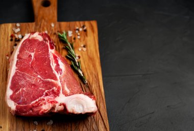 Taş arka plan üzerinde ahşap doğrama tahtası üzerinde baharat ve biberiye dal ile Çiğ yağlı biftek