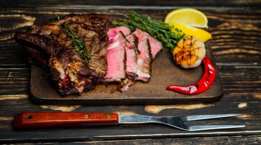 Taze kavrulmuş biftek ahşap doğrama tahtası üzerinde limon dilimleri ve ızgara sarımsak ile servis
