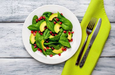 Ahşap masada ıspanak yaprakları, avokado dilimleri ve nar taneleri ile taze yeşil salata 