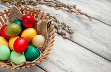 Beyaz ahşap arka planda renkli Paskalya yumurtaları ve kedi söğüt dalları ile sepet
