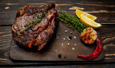 Taze kavrulmuş biftek ahşap doğrama tahtası üzerinde limon dilimleri ve ızgara sarımsak ile servis