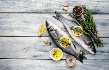 Gri ahşap arka plan üzerinde limon dilimleri ve biberiye dalları ile çiğ balık