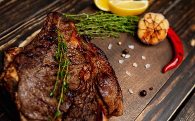 Taze kavrulmuş biftek ahşap doğrama tahtası üzerinde limon dilimleri ve ızgara sarımsak ile servis