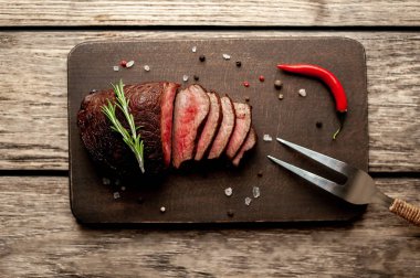 Ahşap arka planda baharat ve biberiye dalları ile taze ızgara biftek